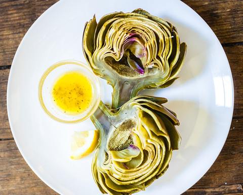 Illustrative photo: A steamed artichoke on a white plate with a small dish of butter and lemon