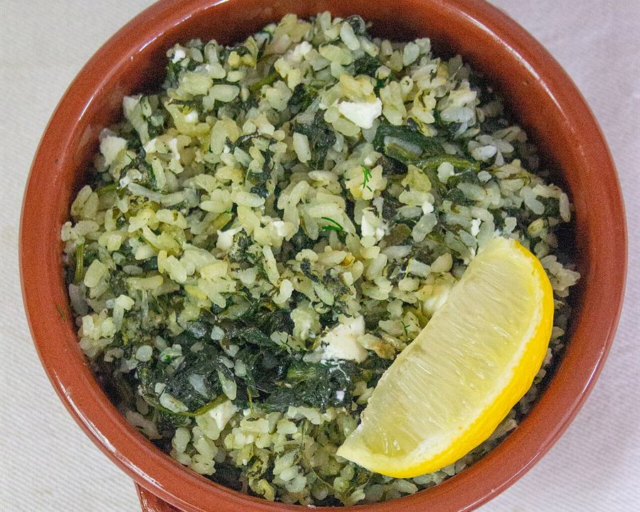 Illustrative photo: Greek spinach rice (spanakorizo) in a terracotta dish with a lemon wedge