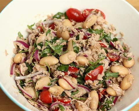 Illustrative photo: A white bowl of white bean and tuna salad with red onion, tomato and herbs